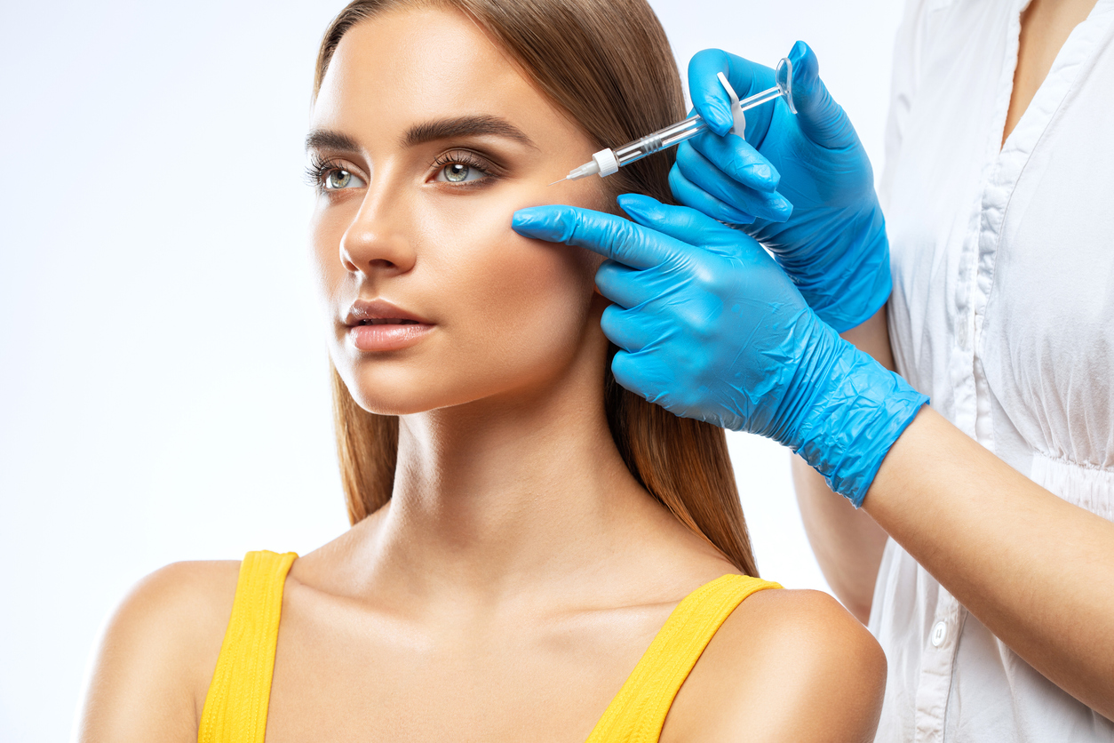 A Gorgeous Woman In A Yellow Tank Top Receives A Dermal Filler Injection From A Nurse In Blue Gloves
