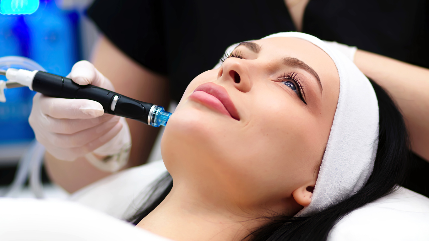 A woman lying down smiling while receiving a HydraFacial skin care treatment at Rodgers Dermatology.