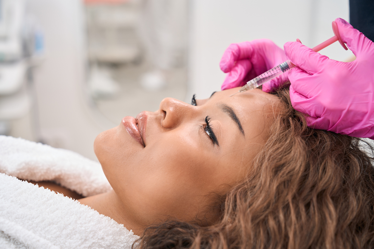 A young woman receiving a botox injection from an esthetician with pink gloves.