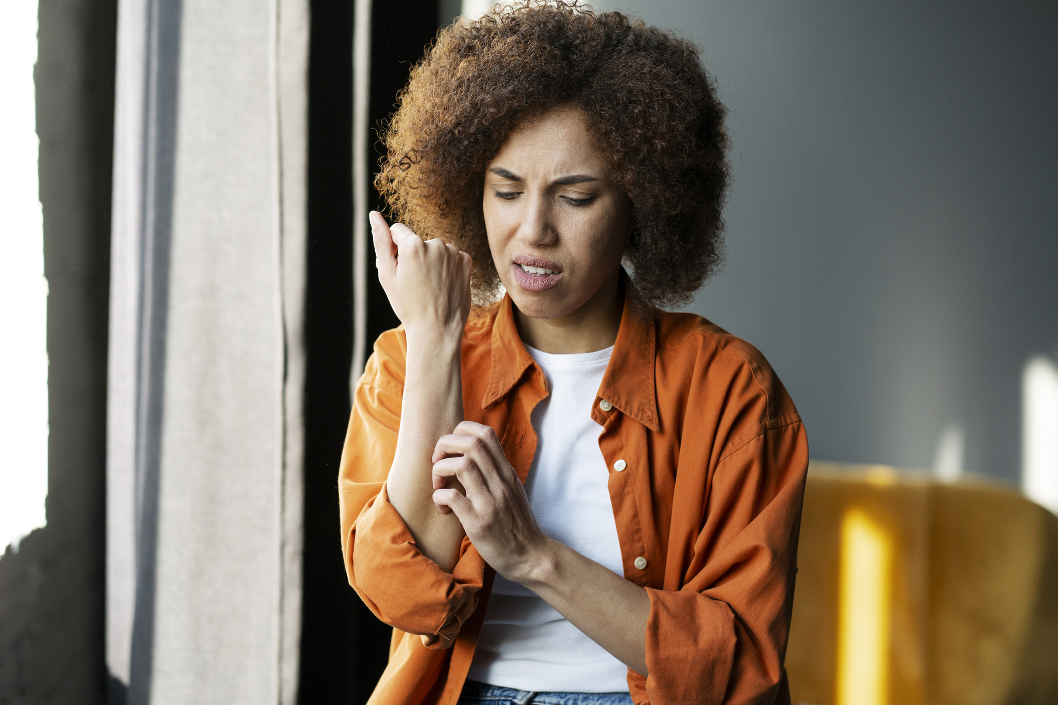 A woman scratches an irritated patch of skin, trying to identify what type of rash is affecting her.