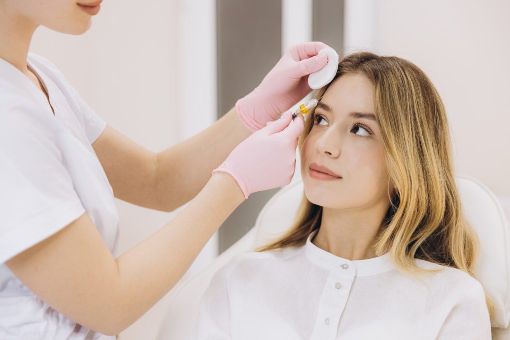 A young woman receiving an HA Filler injectable in her eyebrow by an experienced cosmetic dermatology team member. 